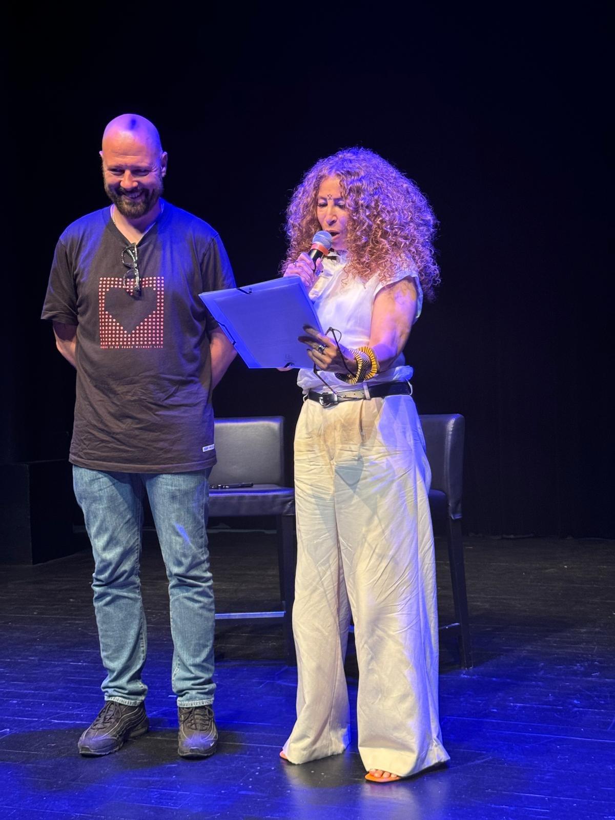 Sur la scène de La Garde, Raïma M., micro et fiches à la main, présente Damien Silvert au public.