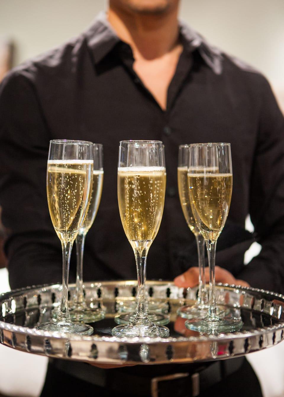 Un serveur en chemise noire présente un plateau d’argent chargé de coupes de champagne.