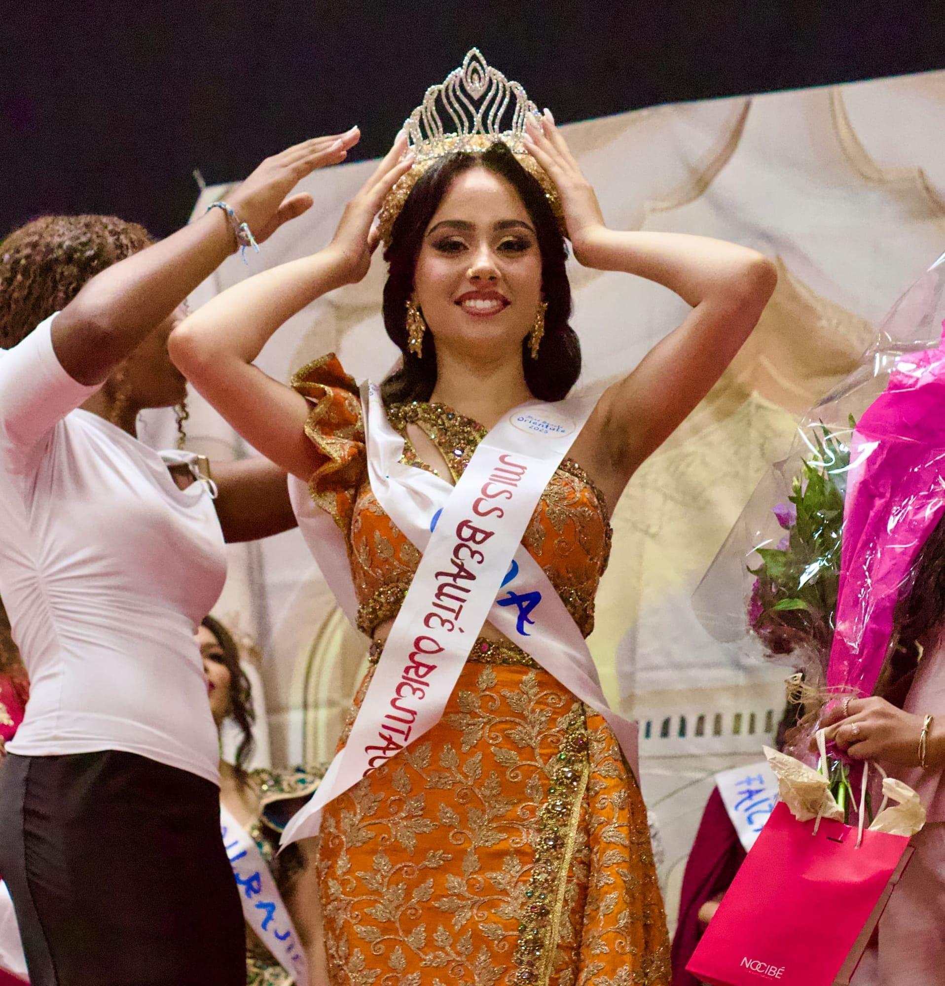 La lauréate de Miss Beauté Orientale 2025, en robe orange et or, ajuste sa couronne sur scène.