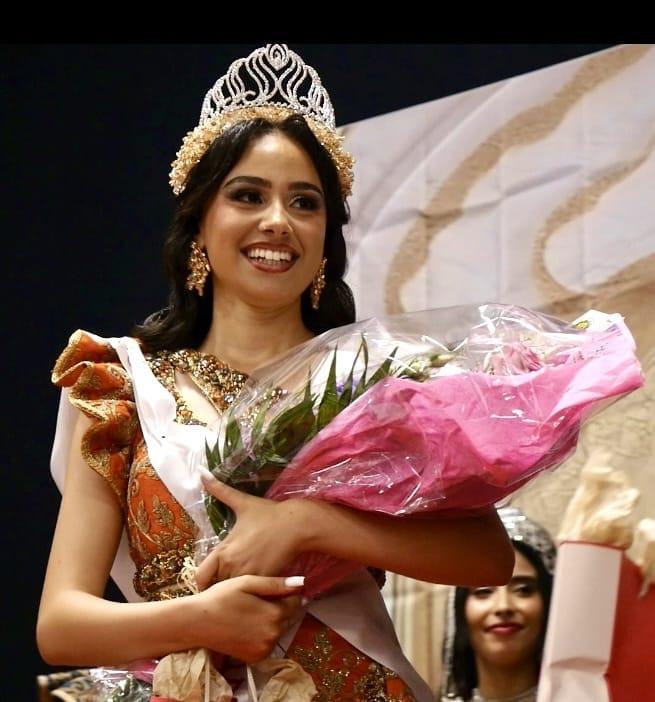 La lauréate couronnée sourit, un grand bouquet de fleurs roses dans les bras.